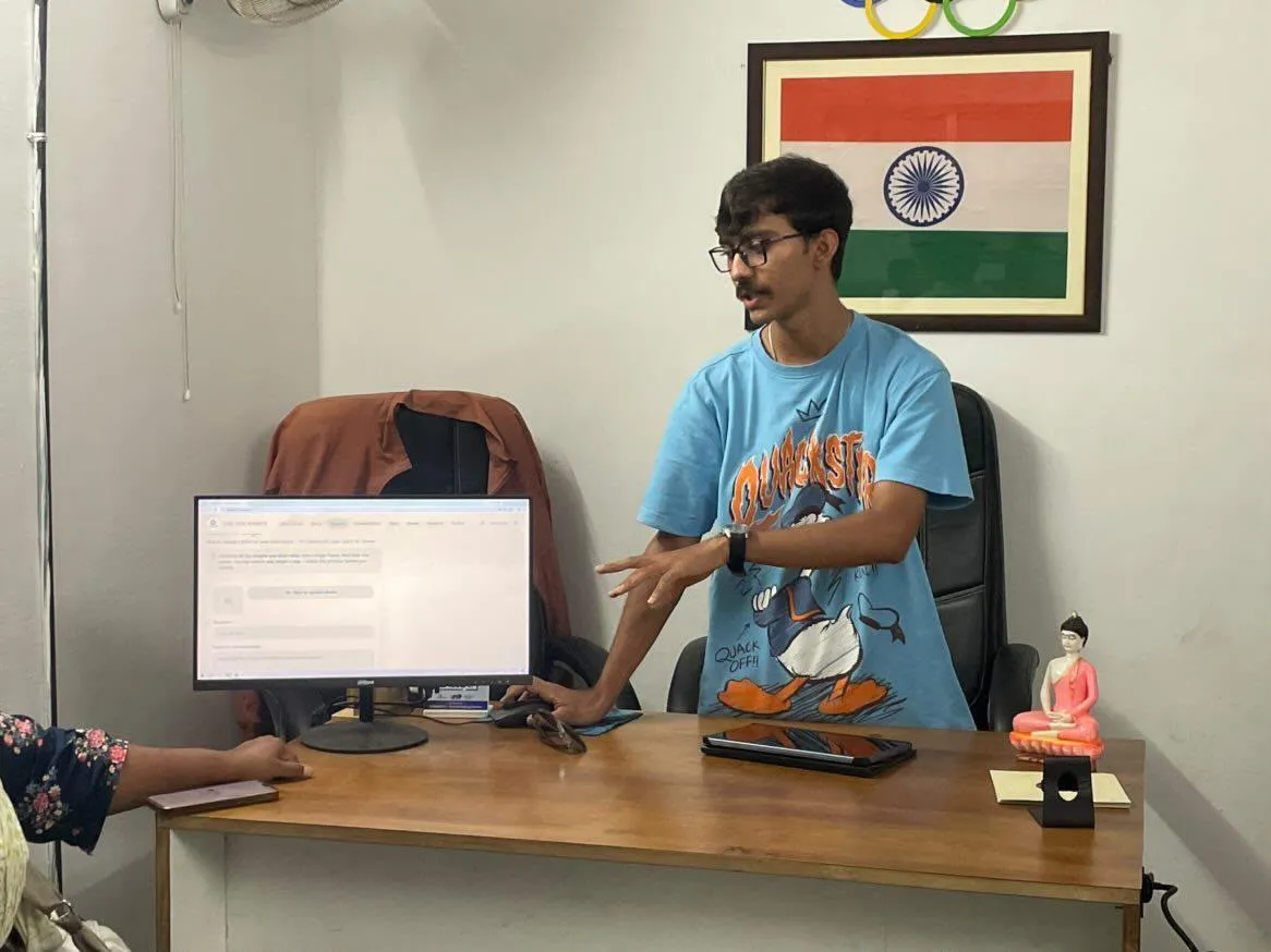 Siddh demoing the Eklavya scoring platform to a coach at the shooting academy — monitor showing the app, Olympic rings and the Indian flag on the wall